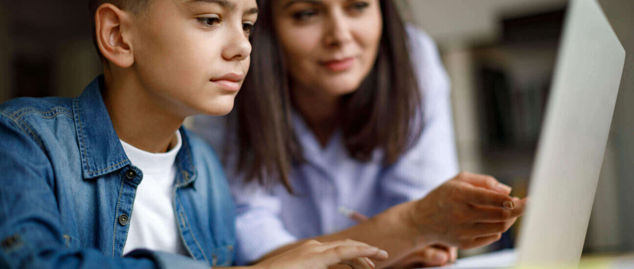 woman leaning over to help child looking at laptop
