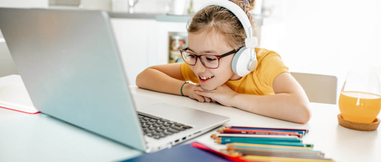 Schoolgirl with headphones and laptop sitting at a desk at home, watching an educational video.