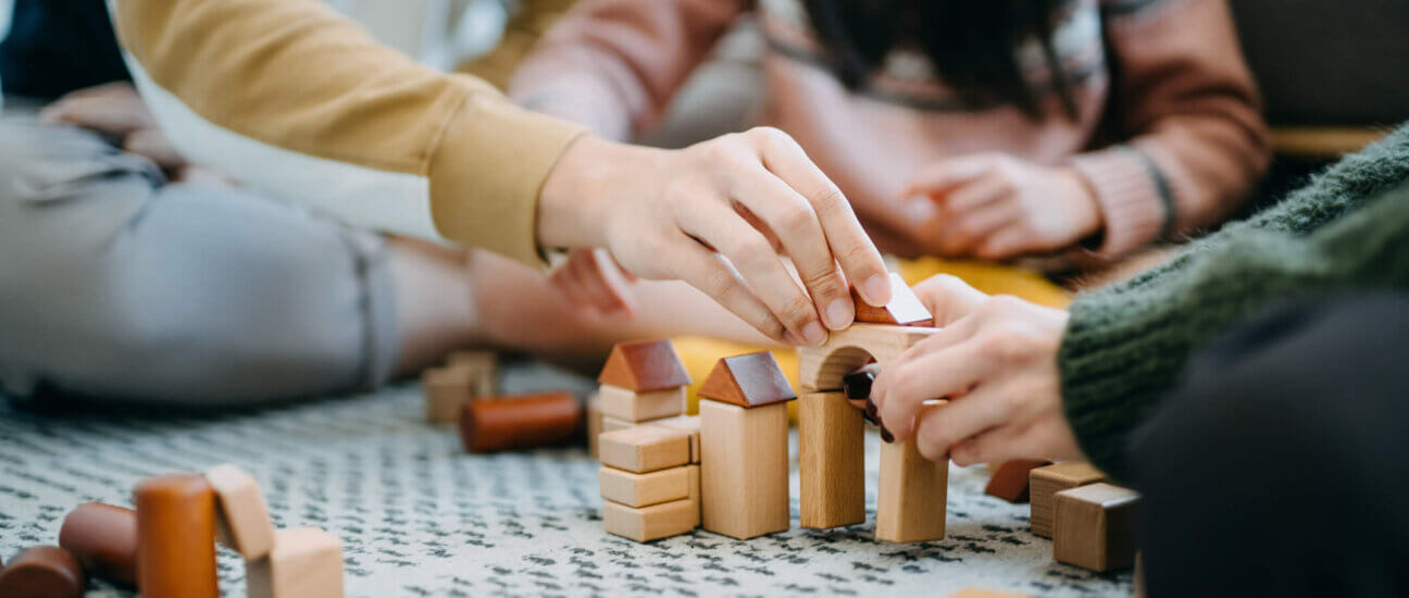 Close up of parents sitting on the floor in the living room playing with wooden building blocks with their daughter