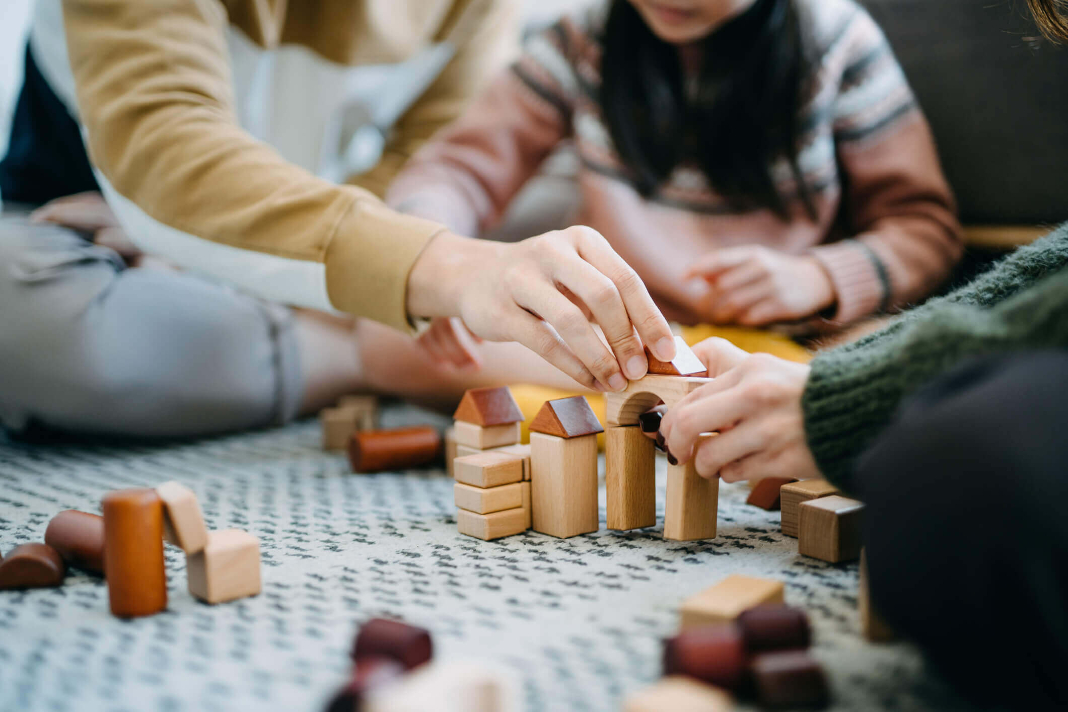 Close up of parents sitting on the floor in the living room playing with wooden building blocks with their daughter