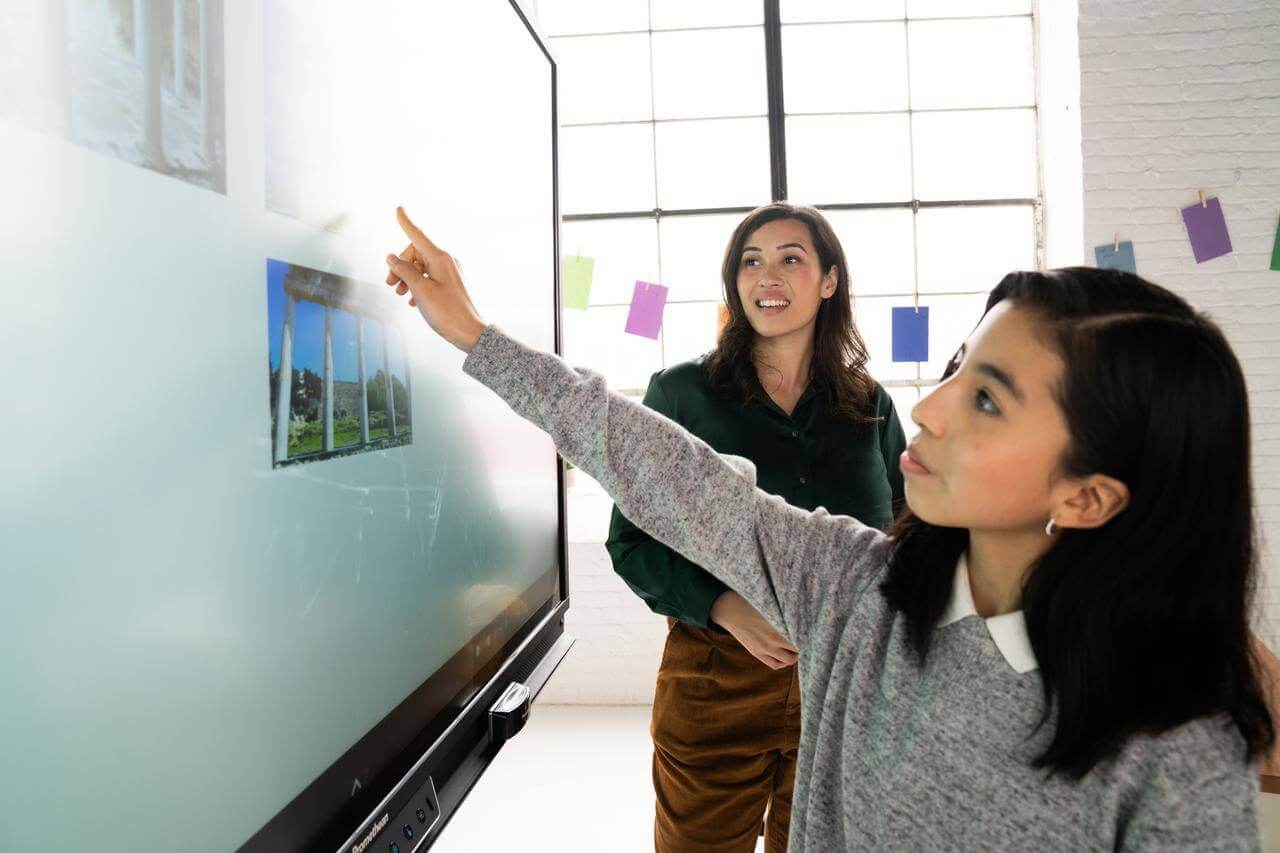Une élève réalise un exercice sur un écran numérique interactif en salle de classe. 