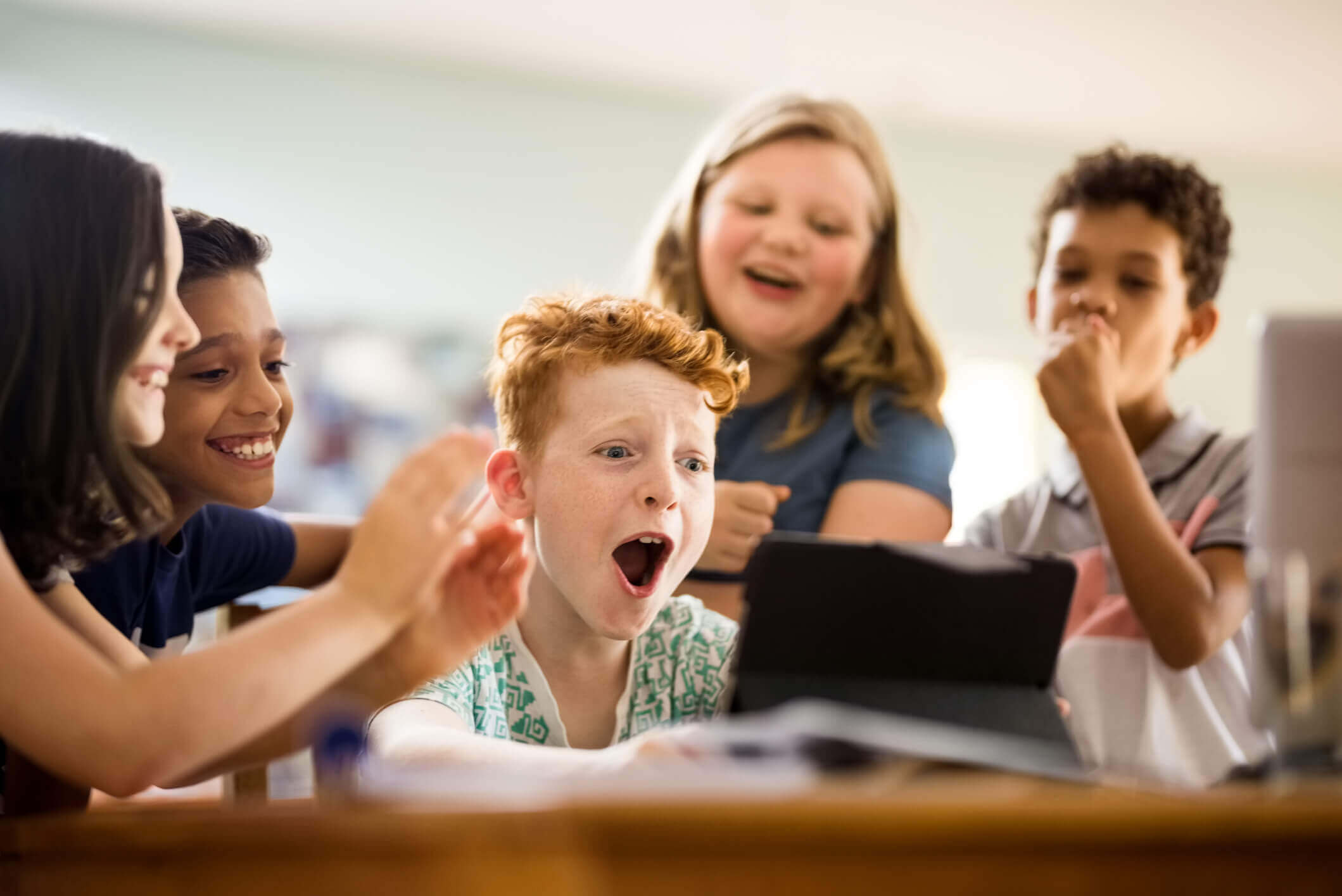 A group of young, excited children learning through play as they use technology in the classroom.
