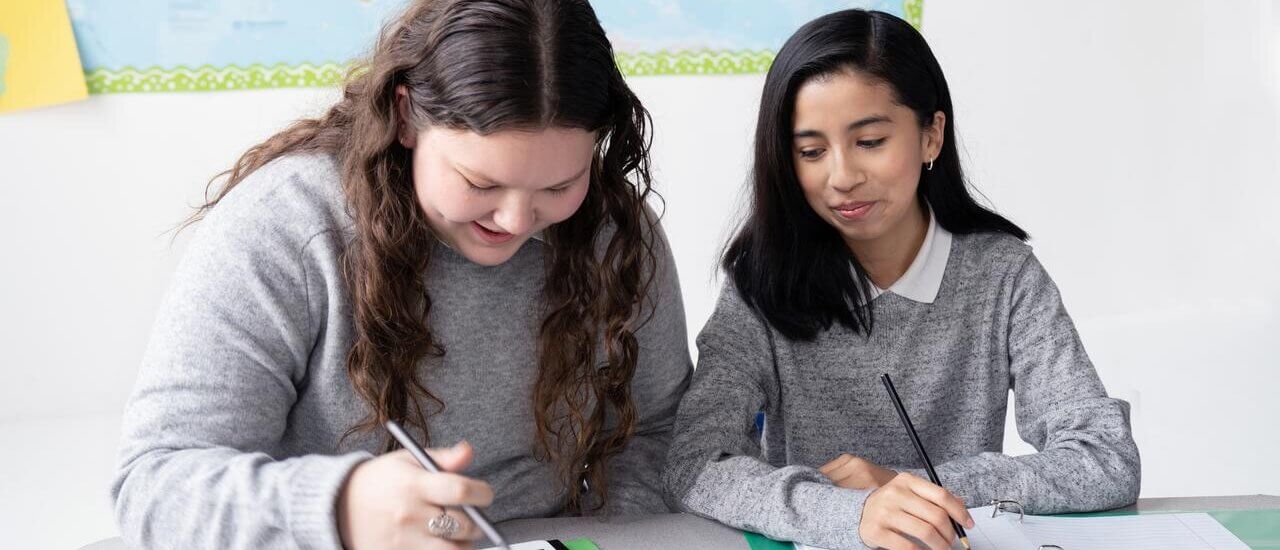 Zwei Kinder sitzen gemeinsam in der Schule um ein Tablet herum.