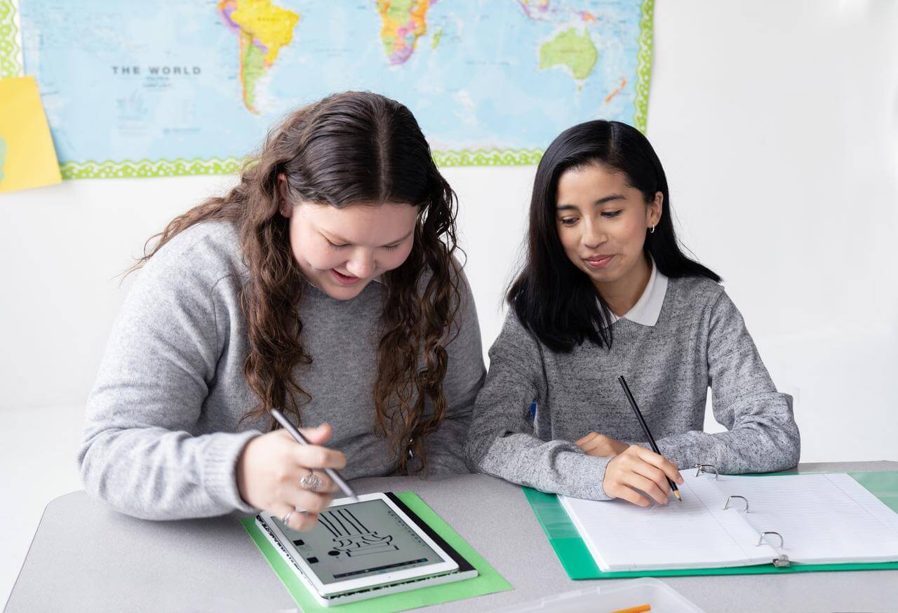Zwei Kinder sitzen gemeinsam in der Schule um ein Tablet herum.