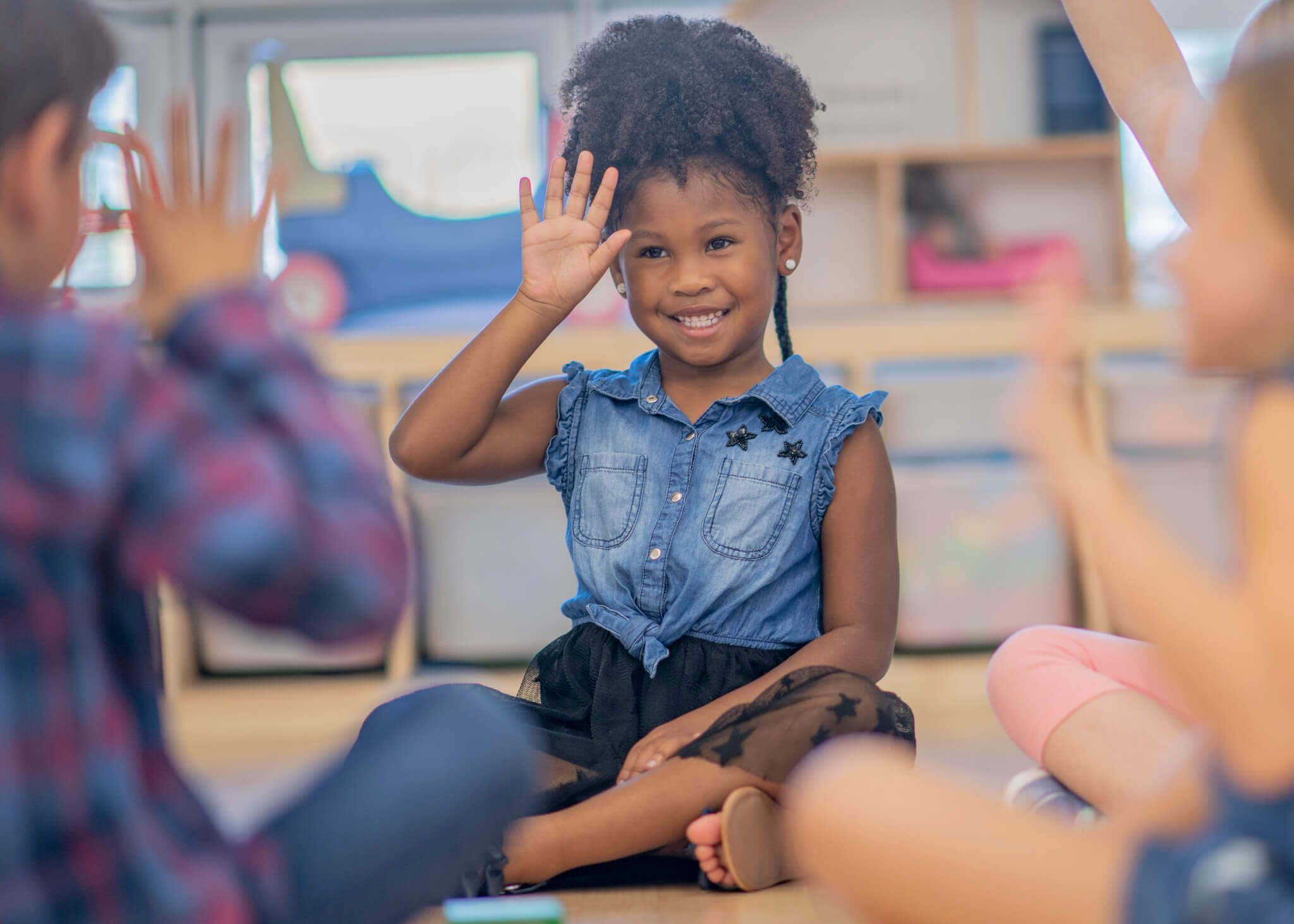 Mädchen sitzt auf dem Boden, umgeben von anderen Kindern und zeigt Gebärdensprache.