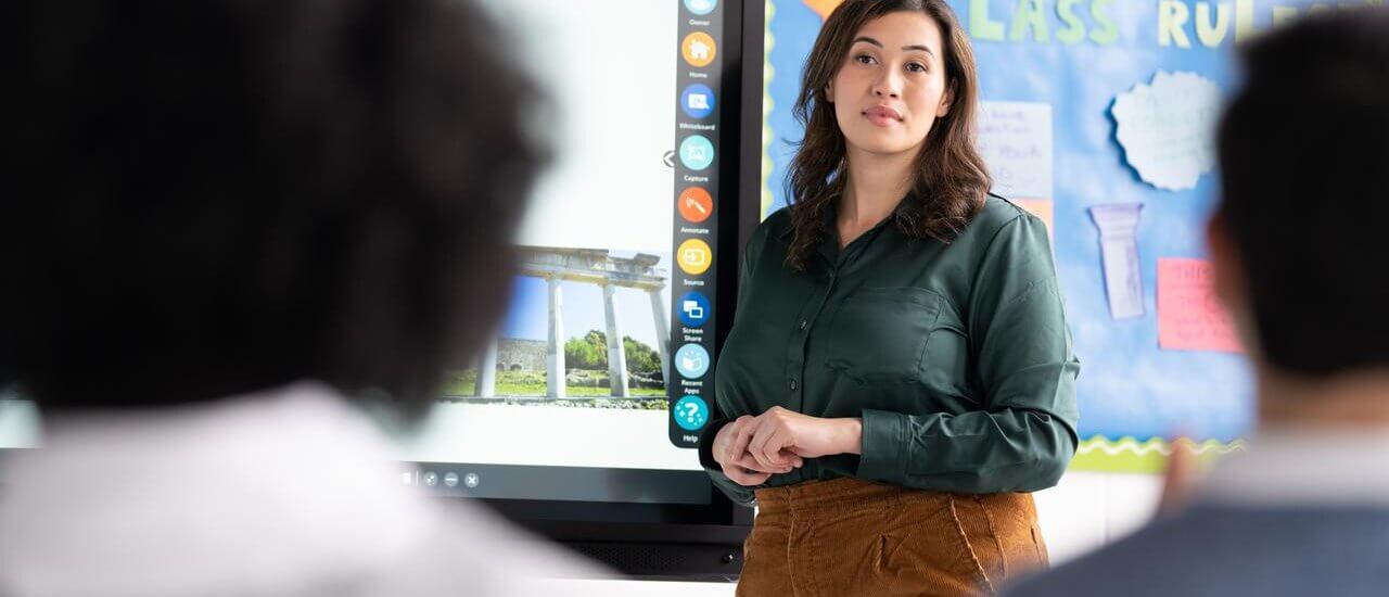 A teacher standing in front of an interactive display looking at her students.