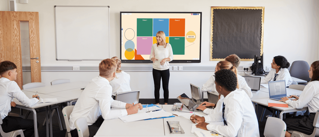 A school teacher presenting to her class standing in front of an interactive display.