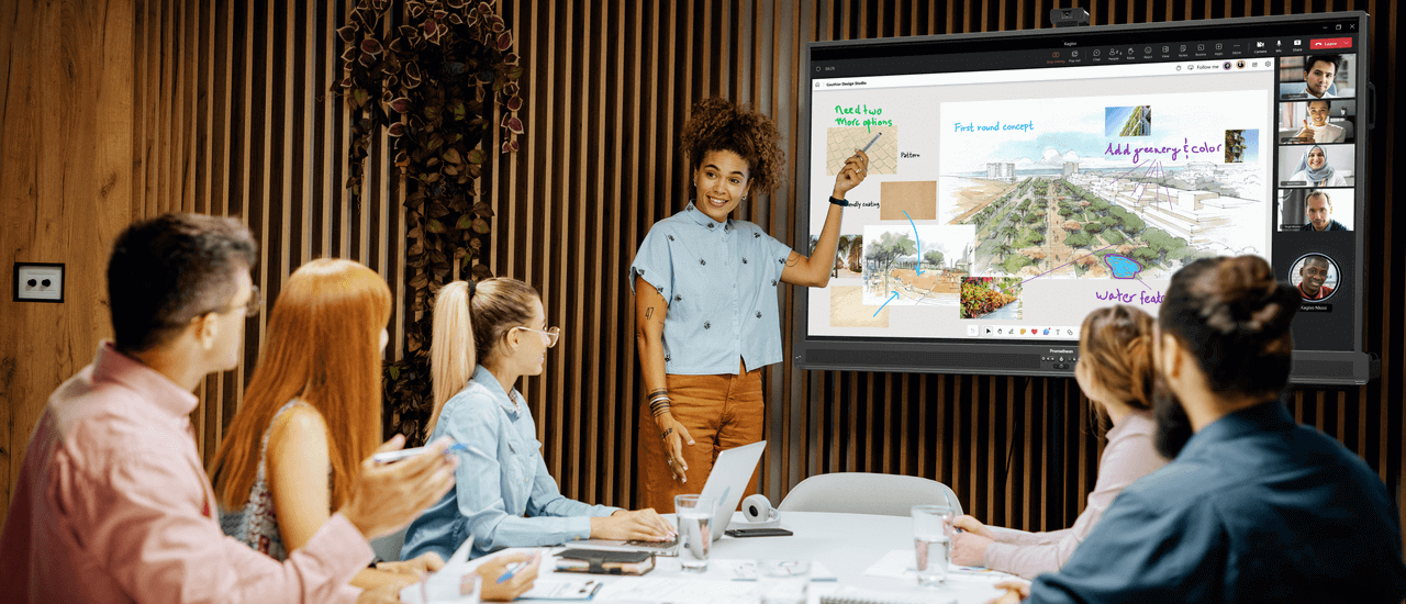 Ein Frau steht vor einem Team an einem digitalen Bildschirm für Präsentationen in einem Meetingraum.