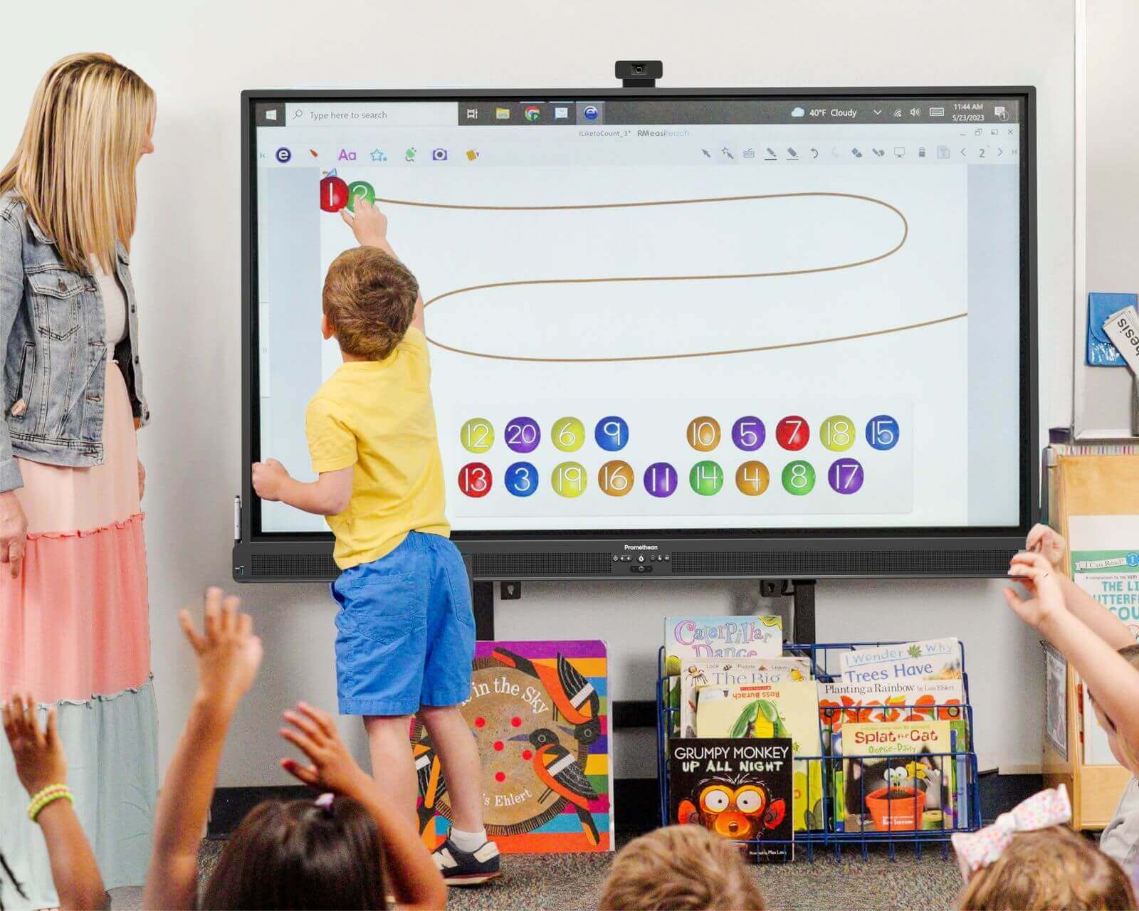 A Pre-K student traces numbers on an ActivPanel running Hatch software while classmates raise their hands
